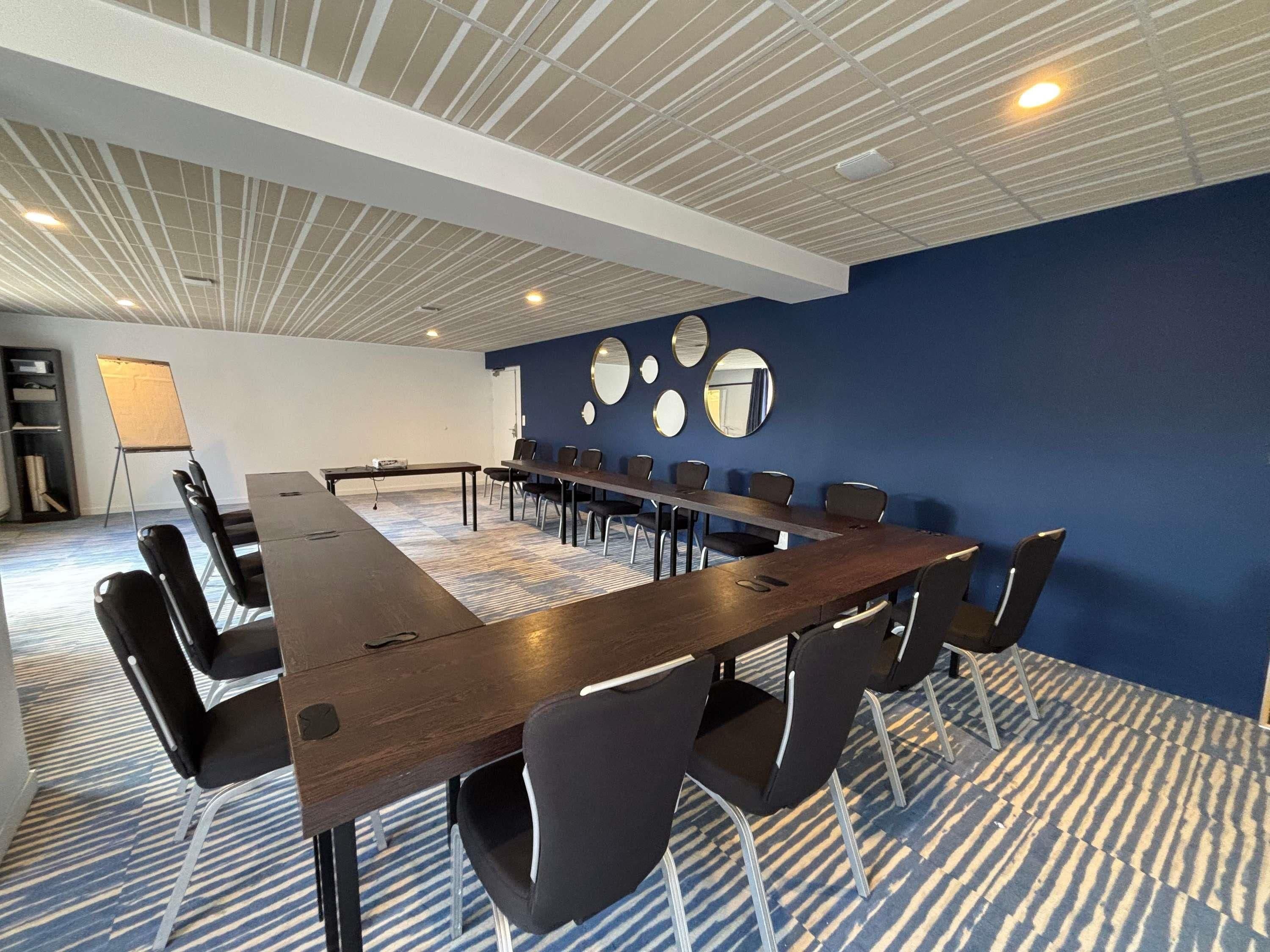 A conference room with a long table and chairs, a whiteboard, and a blue accent wall with circular mirrors.