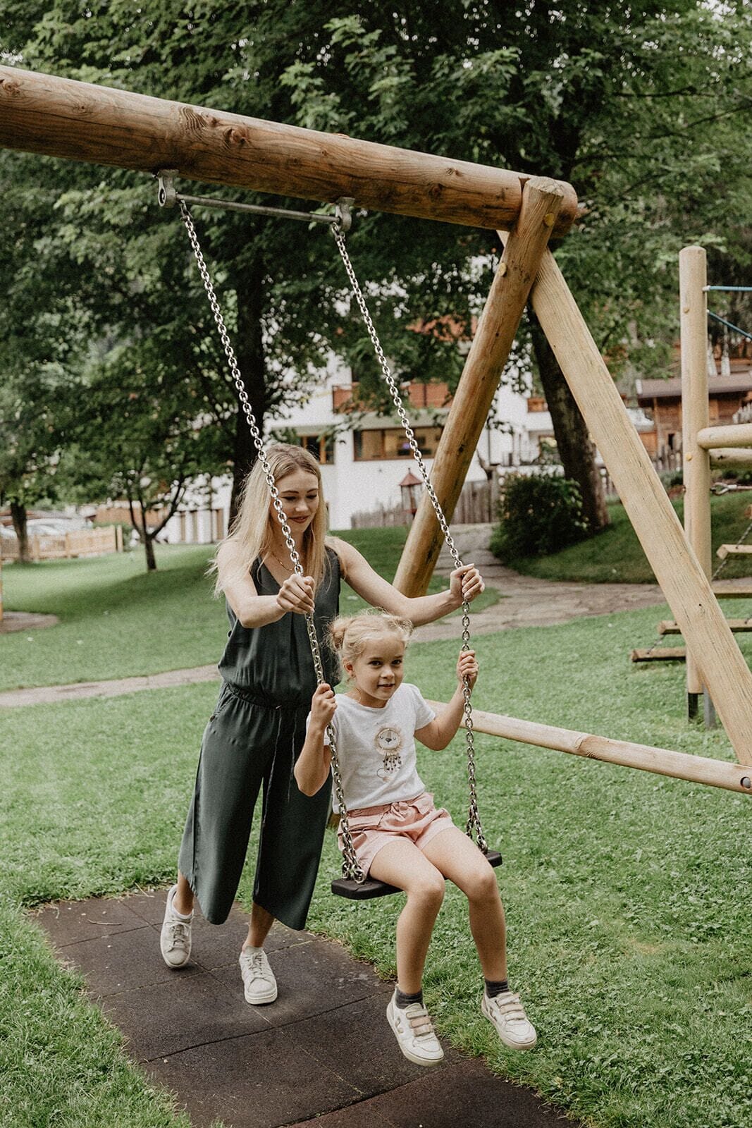 A wooden swing set in a park with a grassy area and trees in the background.
