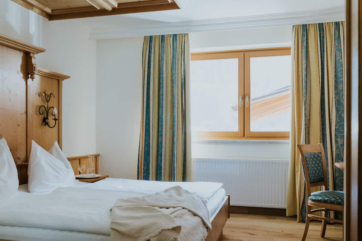 Een hotelkamer met een bed, een houten kledingkast, een stoel en een raam met gordijnen.