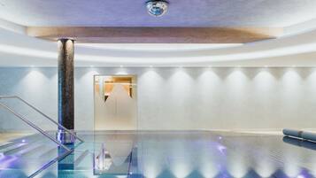 Una piscina interior moderna con suelo de vidrio, una columna central y un diseño minimalista.