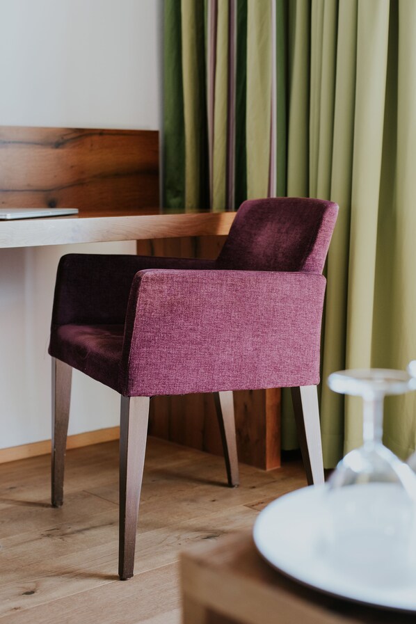 Une chaise recouverte d’un tissu texturé, une table en bois et une chaise blanche dans une pièce dont le sol est en bois et qui est décorée de rideaux verts.