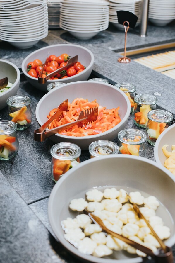 A buffet table with various dishes including a large bowl of shredded carrots, a bowl of cherry tomatoes, and several small jars of pickled vegetables. - Hotel Tauernhof (Grossarl)