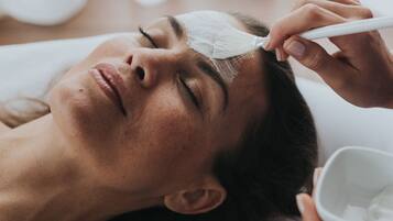 Une personne allongée, la tête couverte d’une serviette blanche, reçoit un soin du visage.