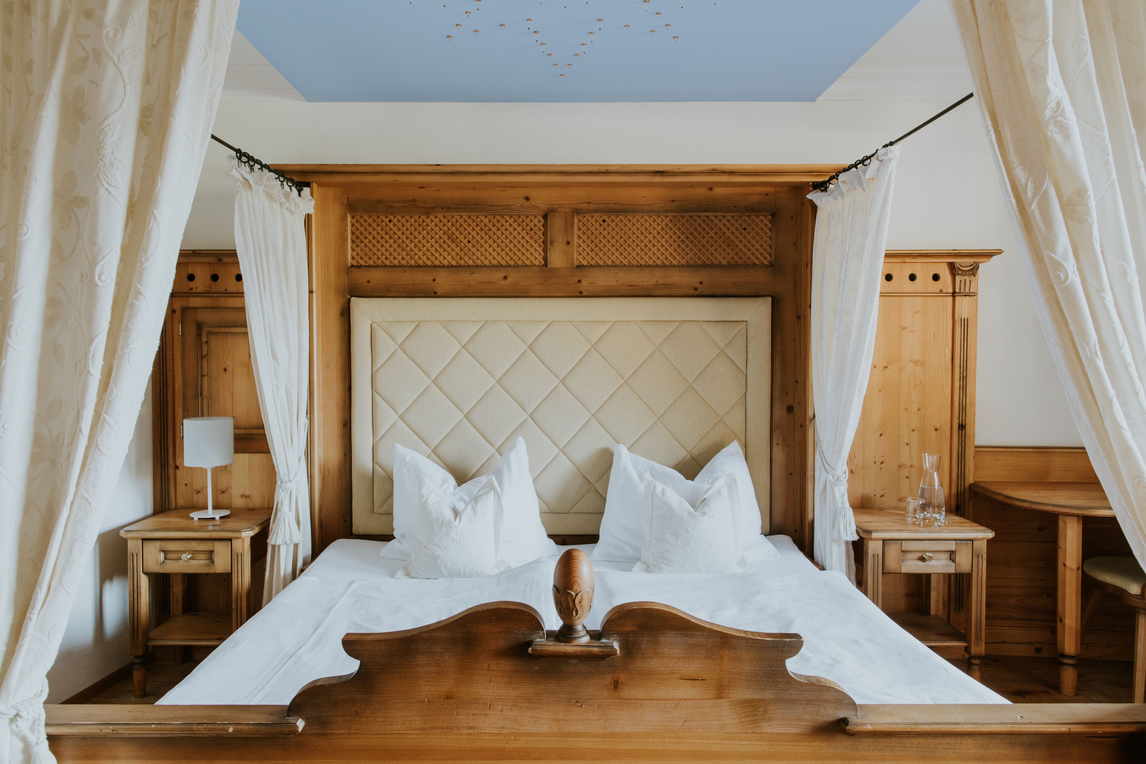 Un dormitorio ordenado con cabecera de madera, cama con ropa blanca y una mesita de noche con lámpara.