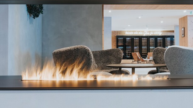 A modern lounge area with a central fire feature, seating, and a visible storefront in the background.