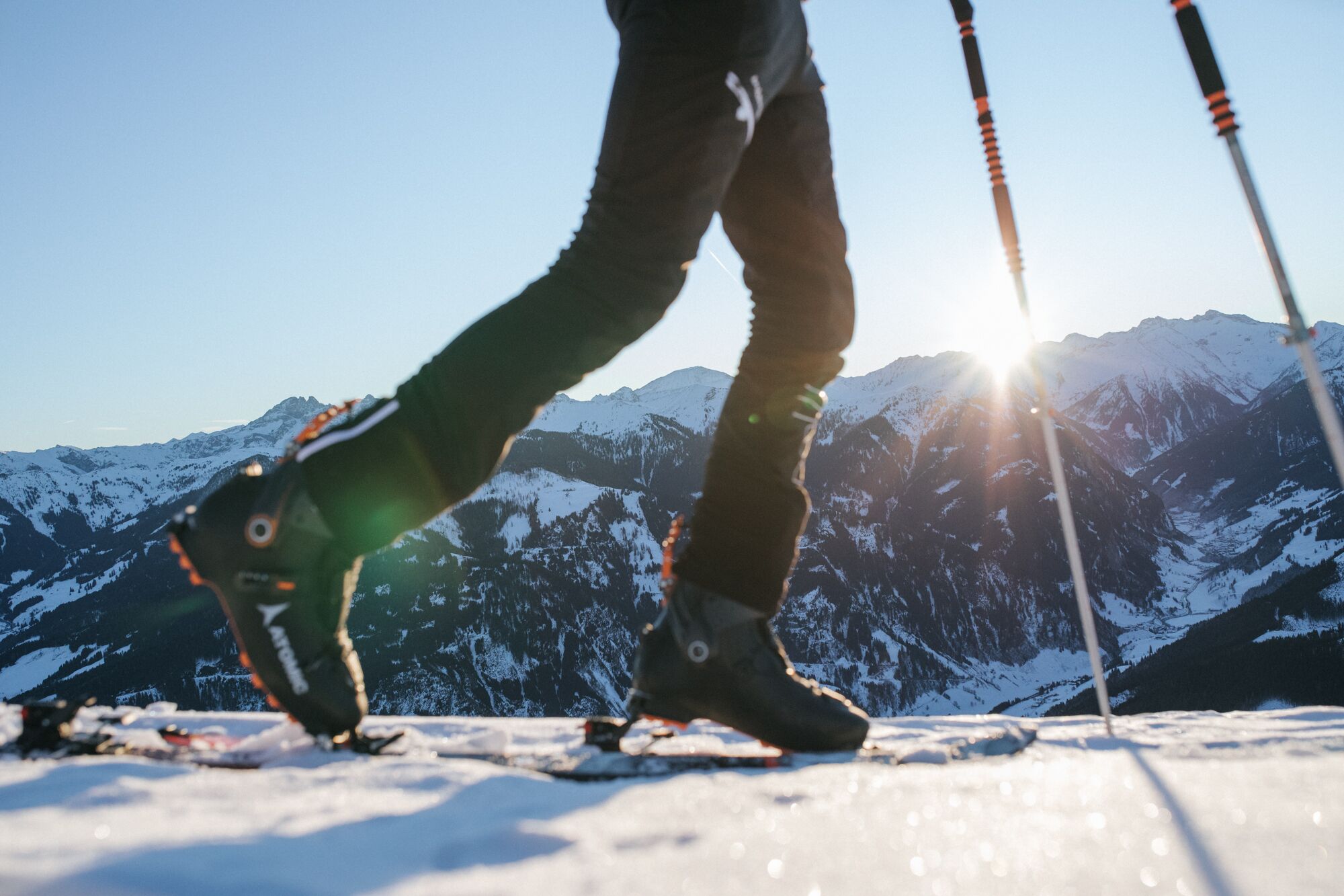 A person skiing with ski poles, with snow-covered mountains in the background and the sun shining.