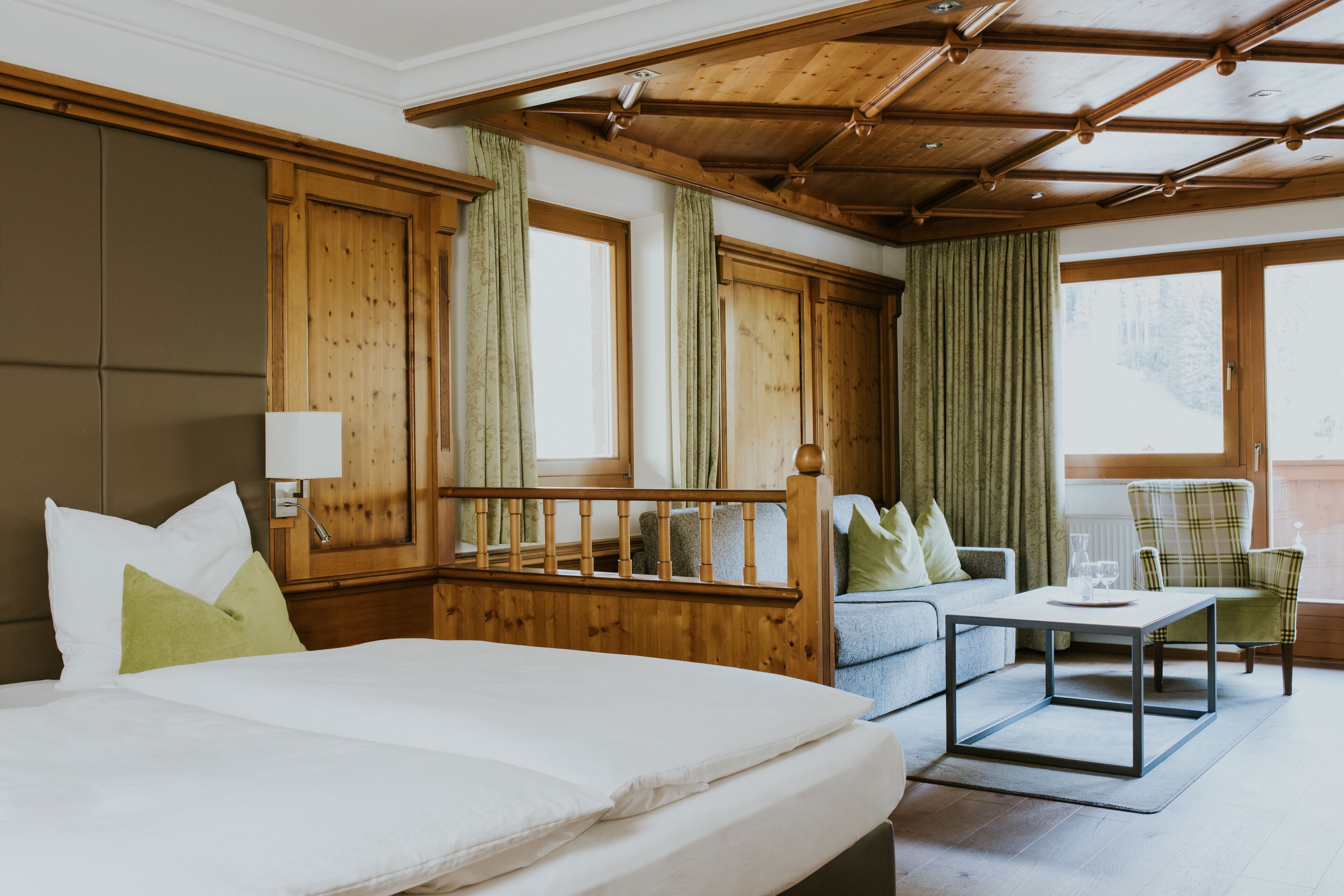 A hotel room with a large bed, a wooden headboard, a sofa, a chair, and a small table.
