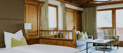 A hotel room with a large bed, a wooden headboard, a sofa, a chair, and a small table.