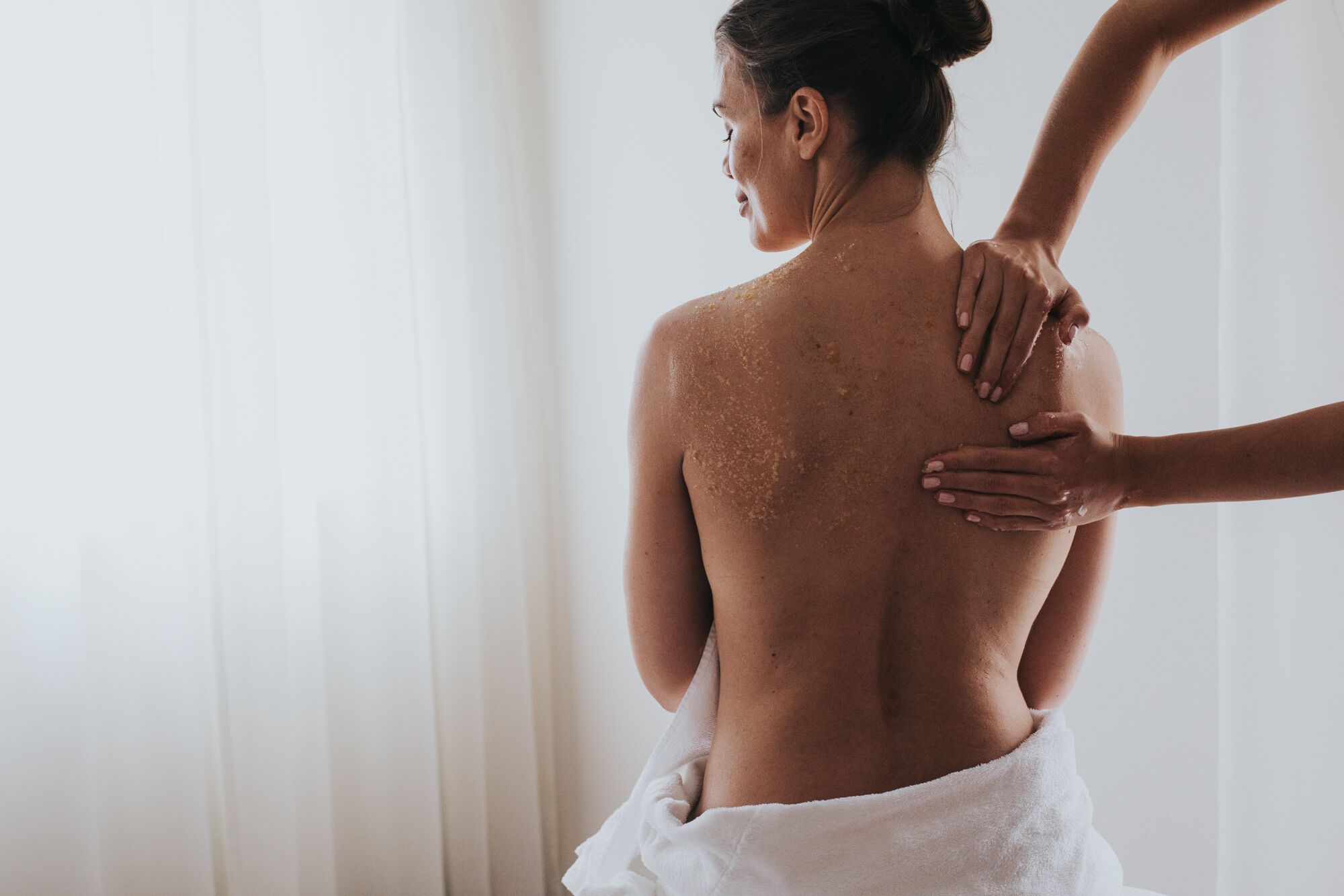 Une personne reçoit un massage du dos dans une pièce dont le fond est constitué d’un simple rideau blanc.
