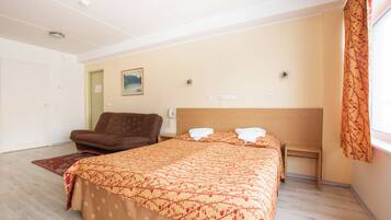 A hotel room with a bed, a chair, a small table, and a window with curtains.