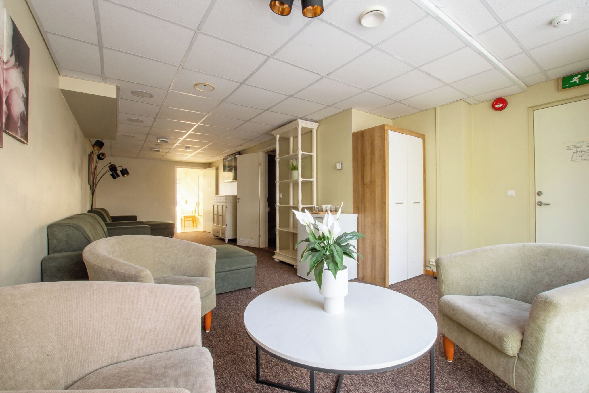 Een hotel lobby met een ronde tafel, twee banken, een kamerplant en een boekenkast.