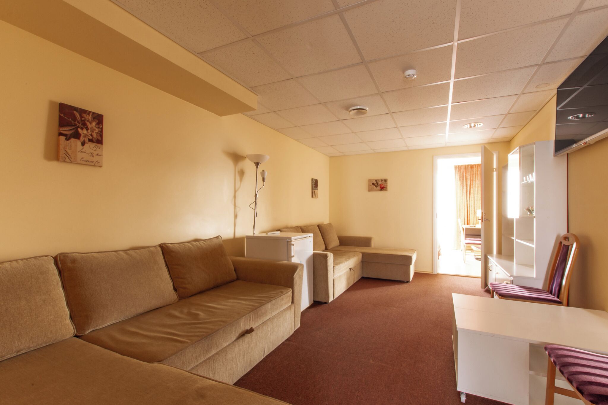 A room with a beige sofa, a small white table, a chair, and a cabinet.