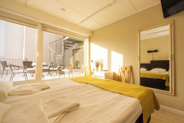 A hotel room with a bed, a large mirror, a desk, and a view of a spiral staircase and outdoor seating area. - Carolina Hotel (Parnu)