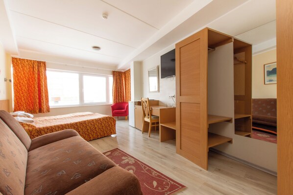 Una habitación con cama, escritorio, silla, televisión y armario.