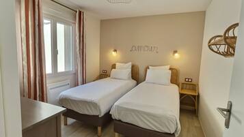 A double room with two beds, a window with curtains, a wall-mounted light, and a ceiling light fixture.