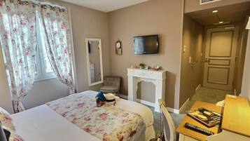 A hotel room with a bed, a desk with a lamp, a television, a mirror, and a fireplace.