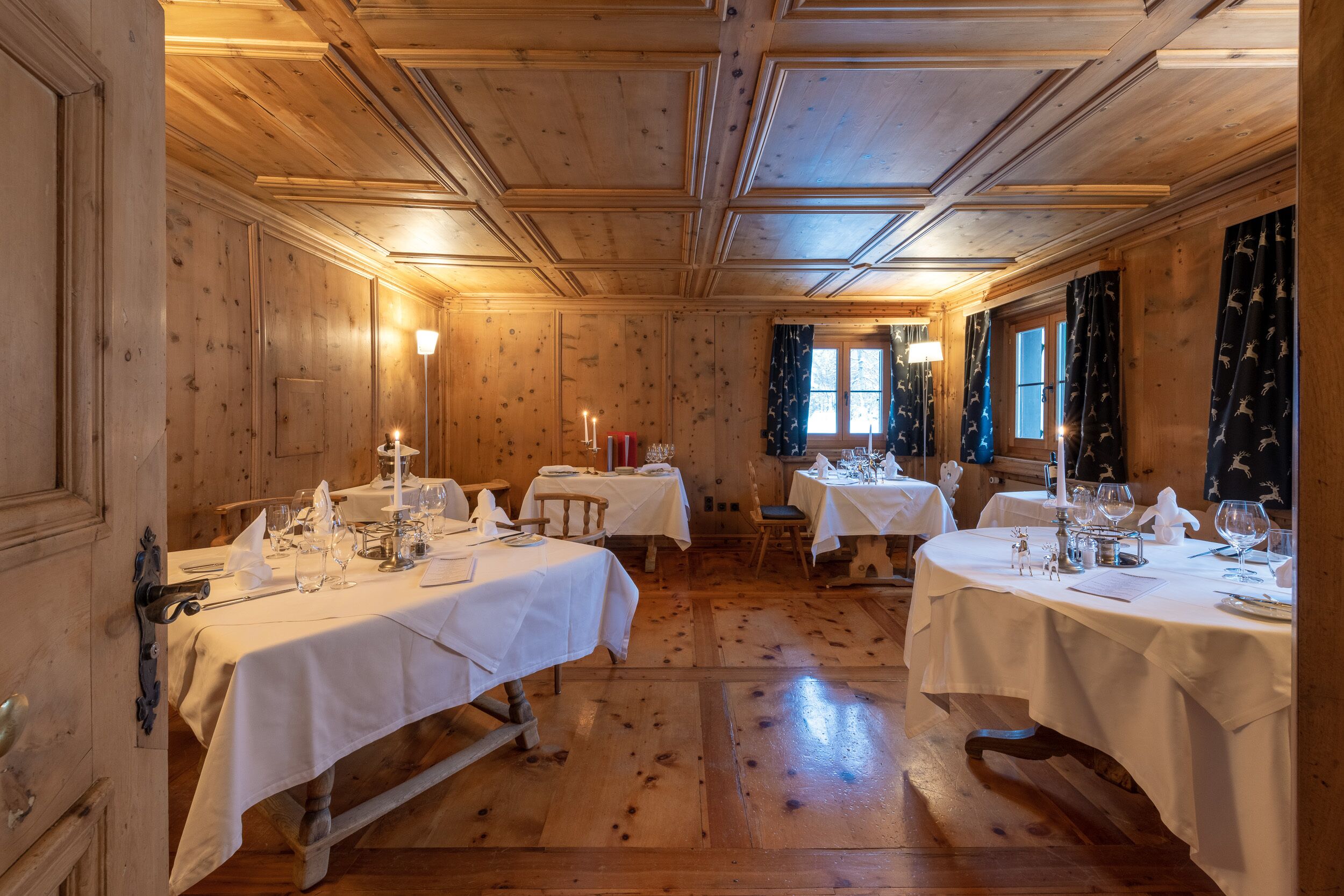 A wooden room with tables set for dining, featuring white tablecloths and candles.
