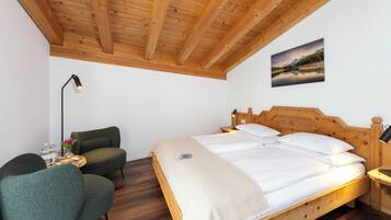 Une pièce avec un plafond en bois, un lit avec une literie blanche, une tête de lit en bois, une table de chevet avec une lampe, un fauteuil vert et un tableau accroché au mur.