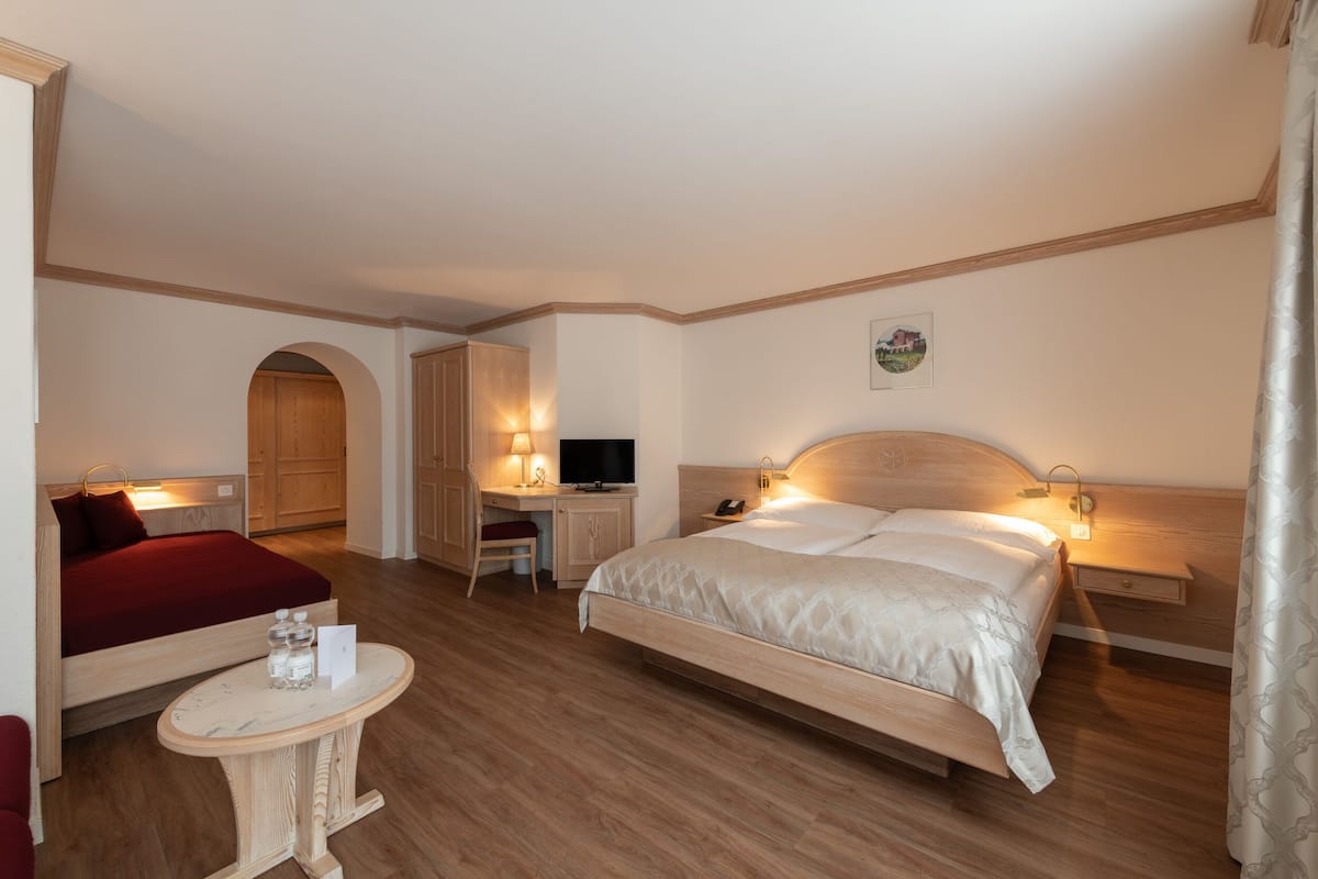 A hotel room with a bed, desk, TV, and a small table with a bottle and glass.