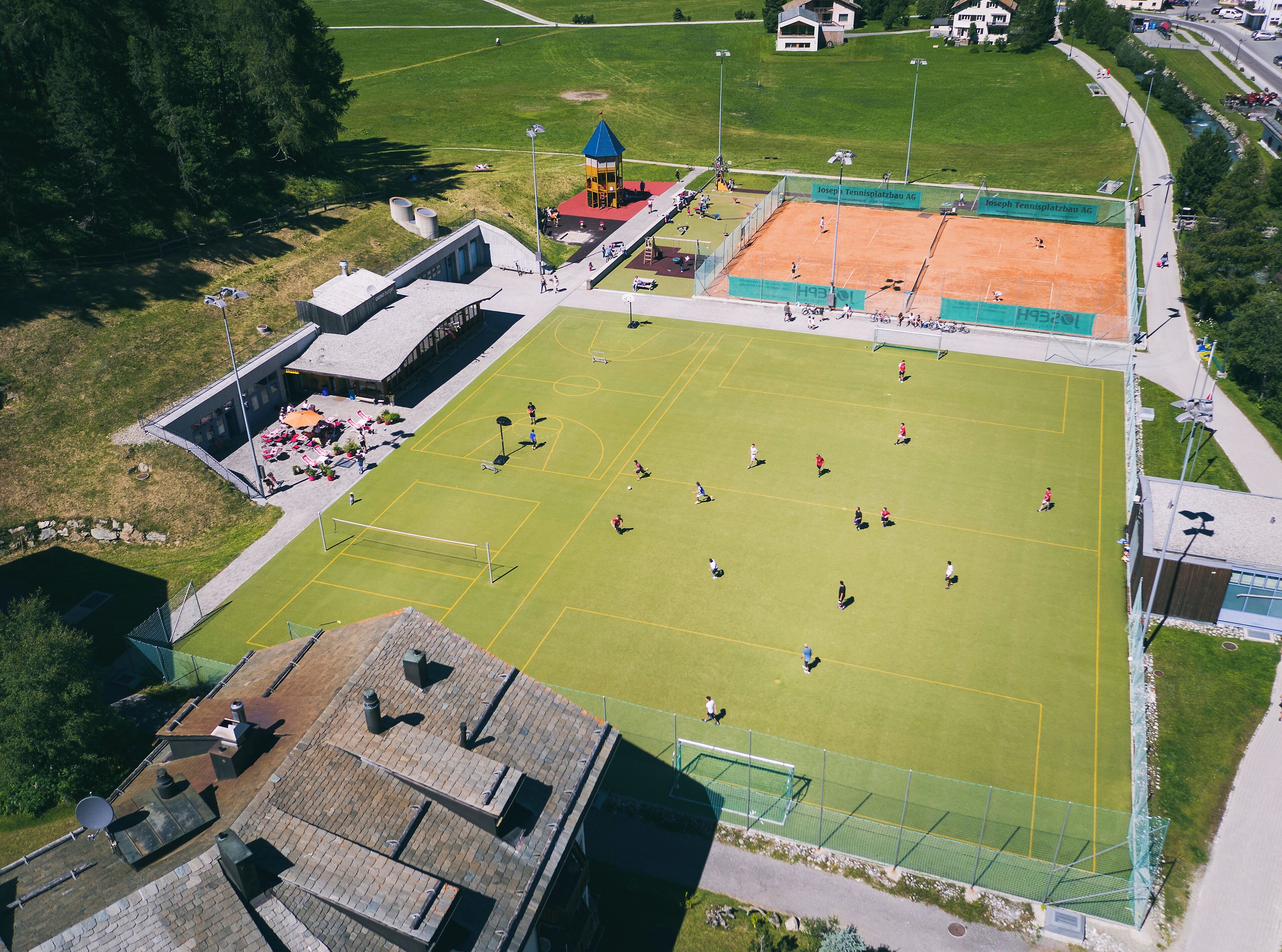 Vista aérea de un complejo deportivo con varias canchas, un pabellón y una valla perimetral.