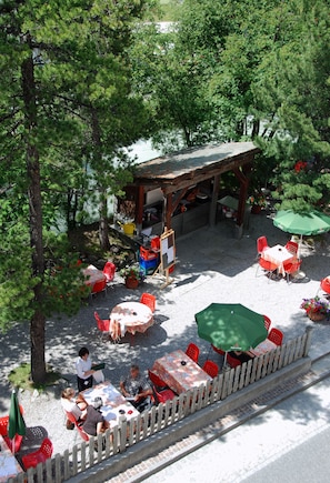 Relax in the serene patio area, surrounded by lush trees and a charming pergola, with comfortable seating and tables for a peaceful retreat.