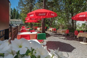 Un espace extérieur aménagé avec des tables et des chaises, des parasols rouges et des fleurs blanches.