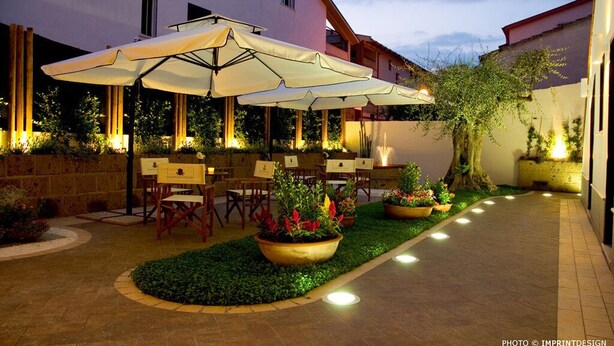 An outdoor patio area with tables and chairs, surrounded by potted plants and illuminated by ground lights. - Residenza Glave - Albergo Diffuso (Campomarino)