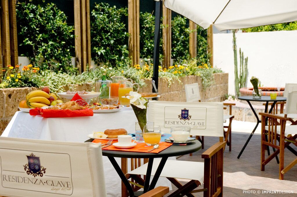 Ein Frühstückstisch mit verschiedenen Speisen und Getränken, umgeben von Stühlen und einer weißen Tischdecke, mit Blick auf einen Garten im Hintergrund.