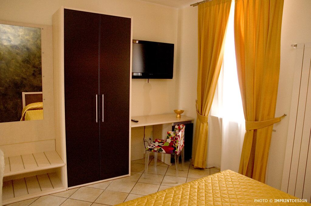 Een slaapkamer met een bed, een kledingkast, een bureau, een stoel, een televisie en gordijnen.