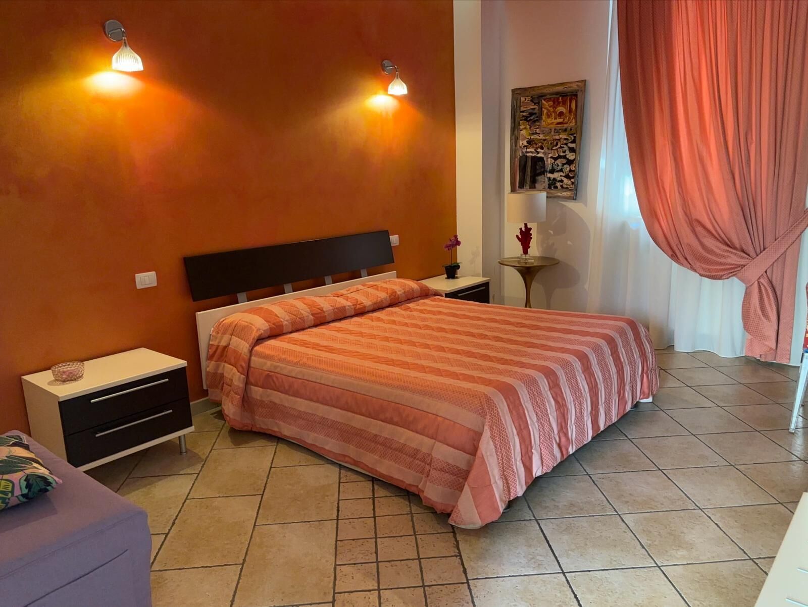 Un dormitorio con cama, mesitas de noche, una pequeña mesa y una lámpara de pared.