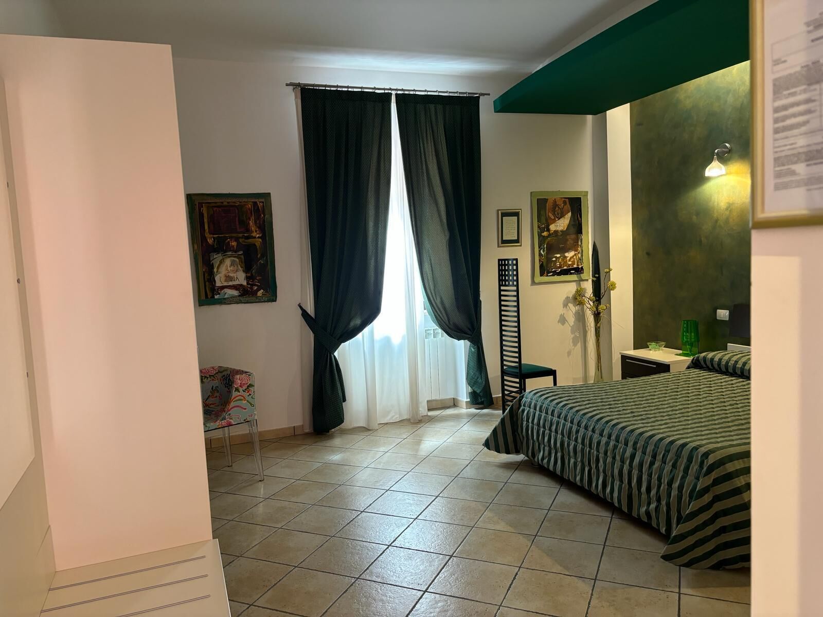 Quarto com cama, cadeira, escrivaninha e janela com cortinas.