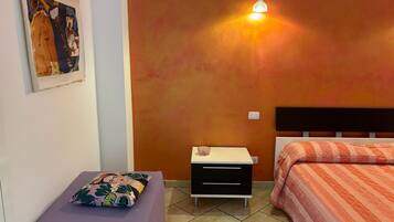 A room with a bed, a nightstand, a small table, and a wall-mounted light fixture.