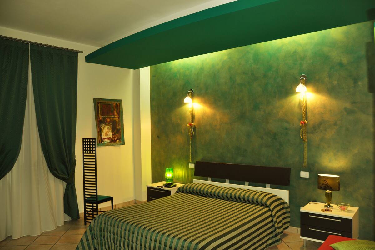 Ein Schlafzimmer mit einem Bett, zwei Nachttischen, einem Beistelltisch, einem Sessel, einer Lampe und einem Bild an der Wand.