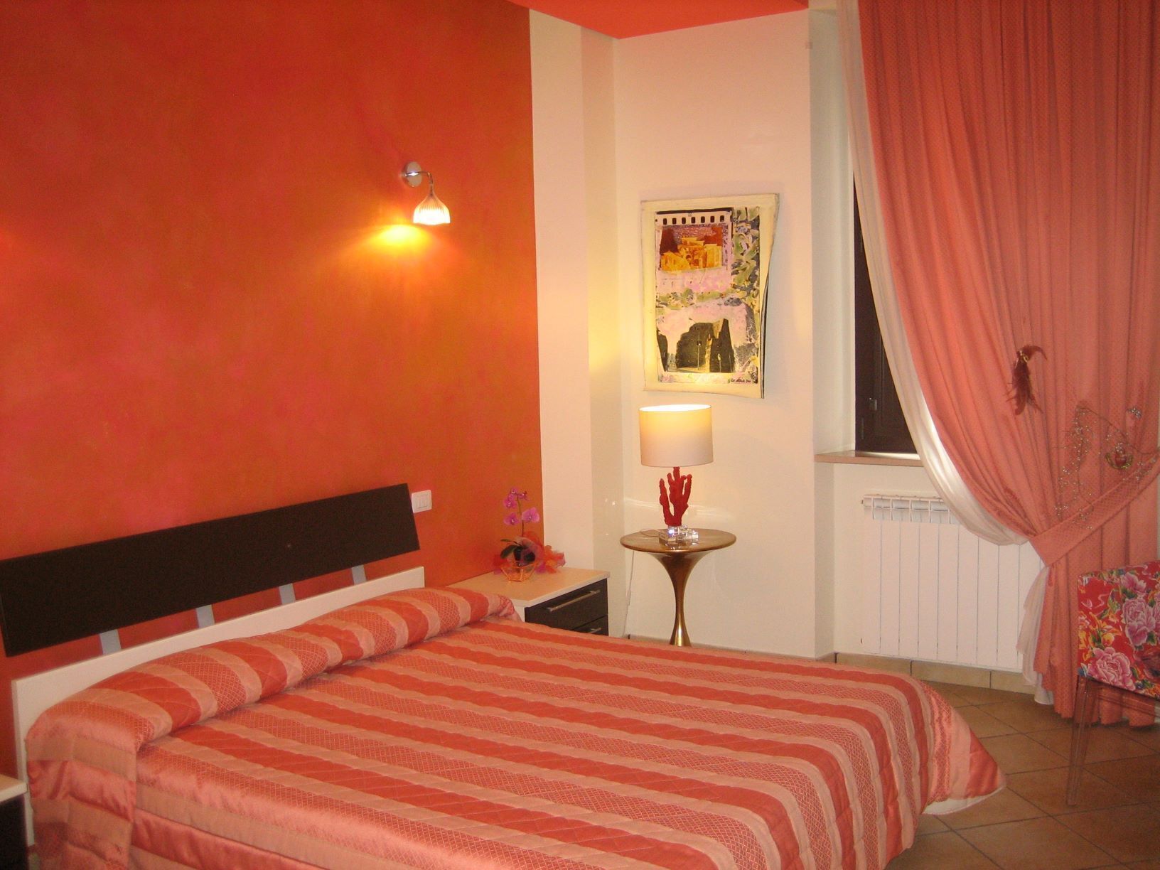 A bedroom with a bed, a nightstand, a lamp, a wall art piece, and a window with curtains.