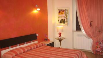 A bedroom with a bed, a nightstand, a lamp, a wall art piece, and a window with curtains.