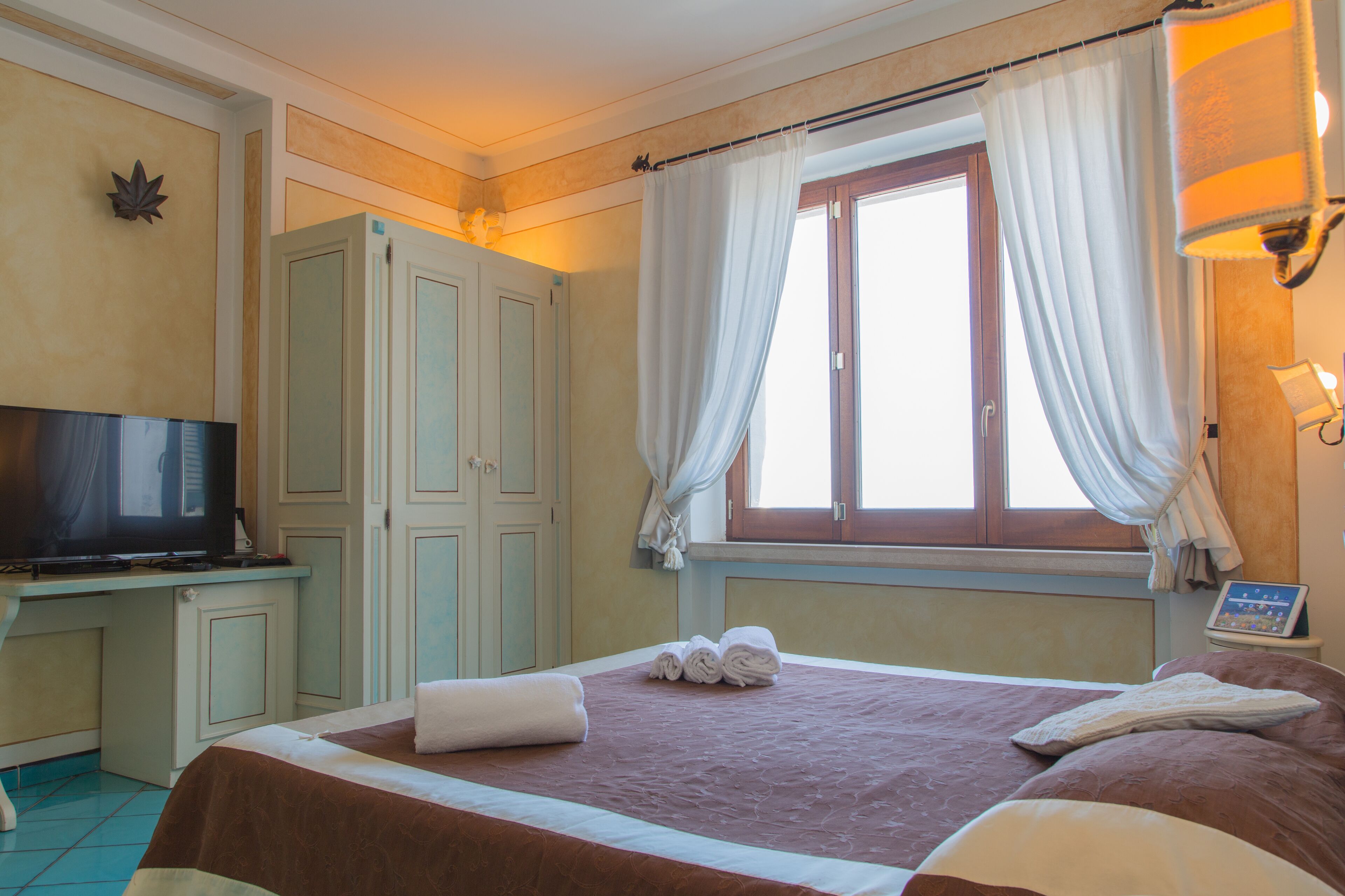 A hotel room with a bed, a television, a desk, and a window with curtains.