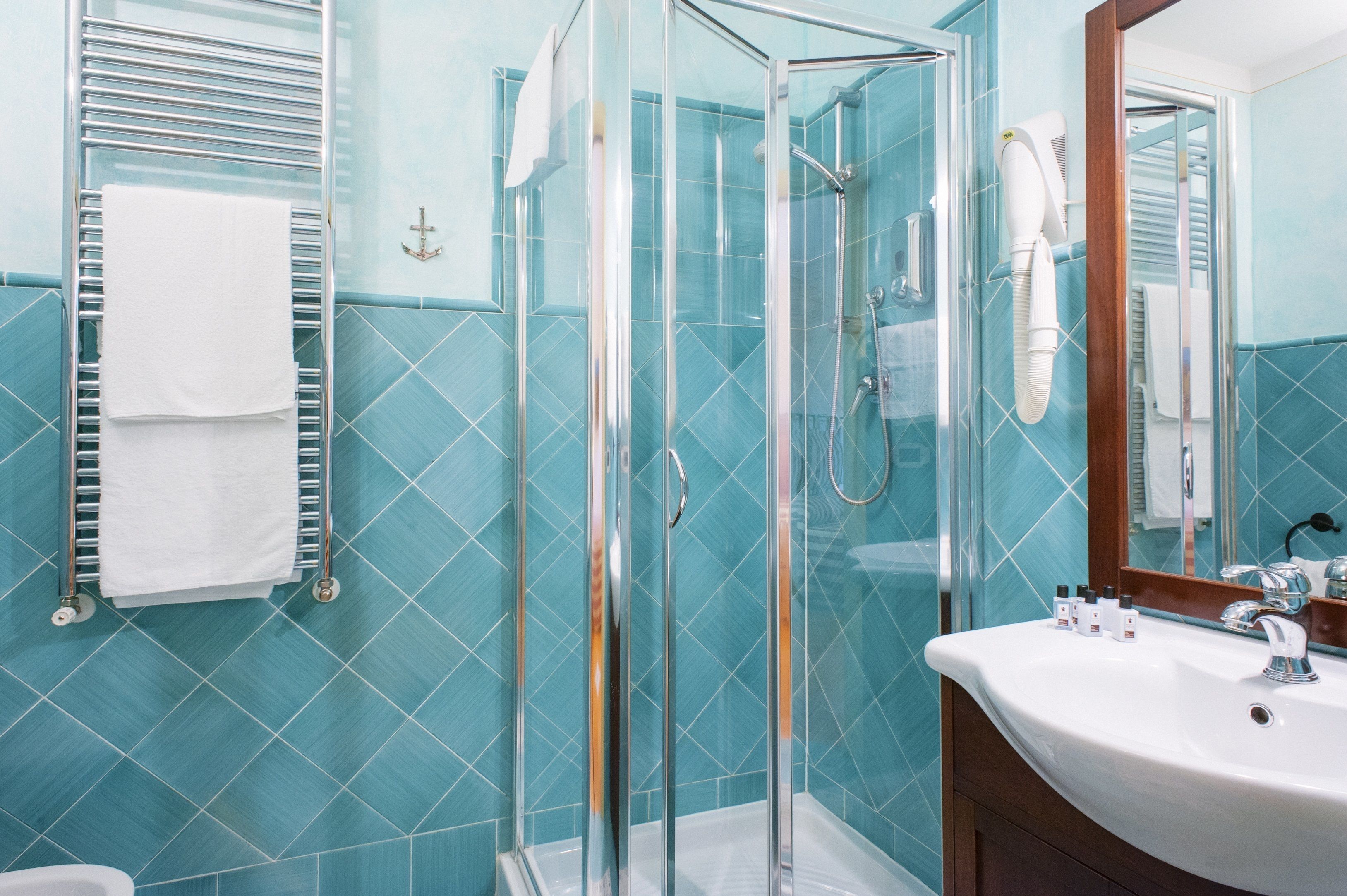 A bathroom with a glass shower enclosure, a white sink, and a towel rack with a white towel.