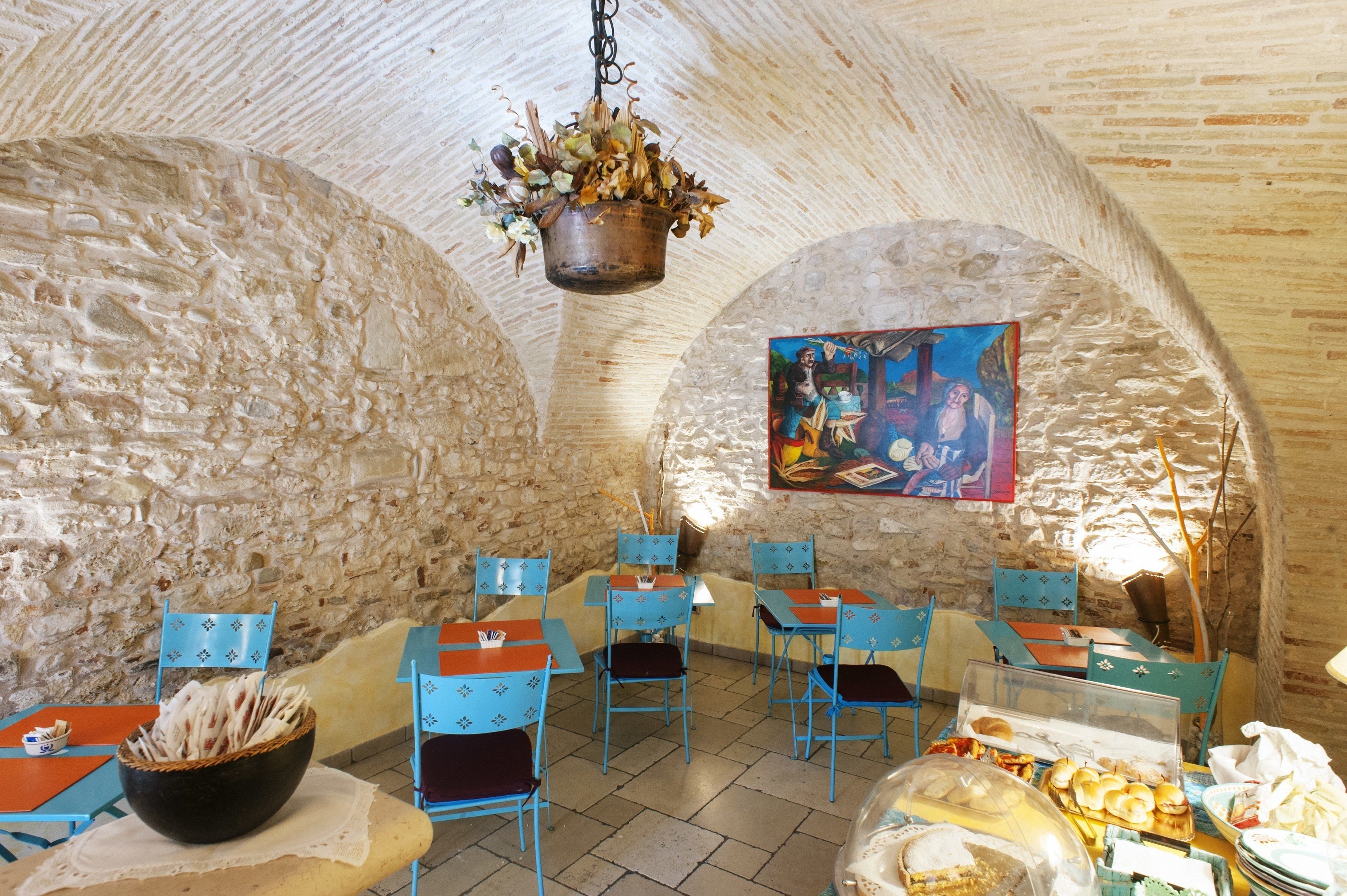 A rustic interior with stone walls, blue chairs, and tables.