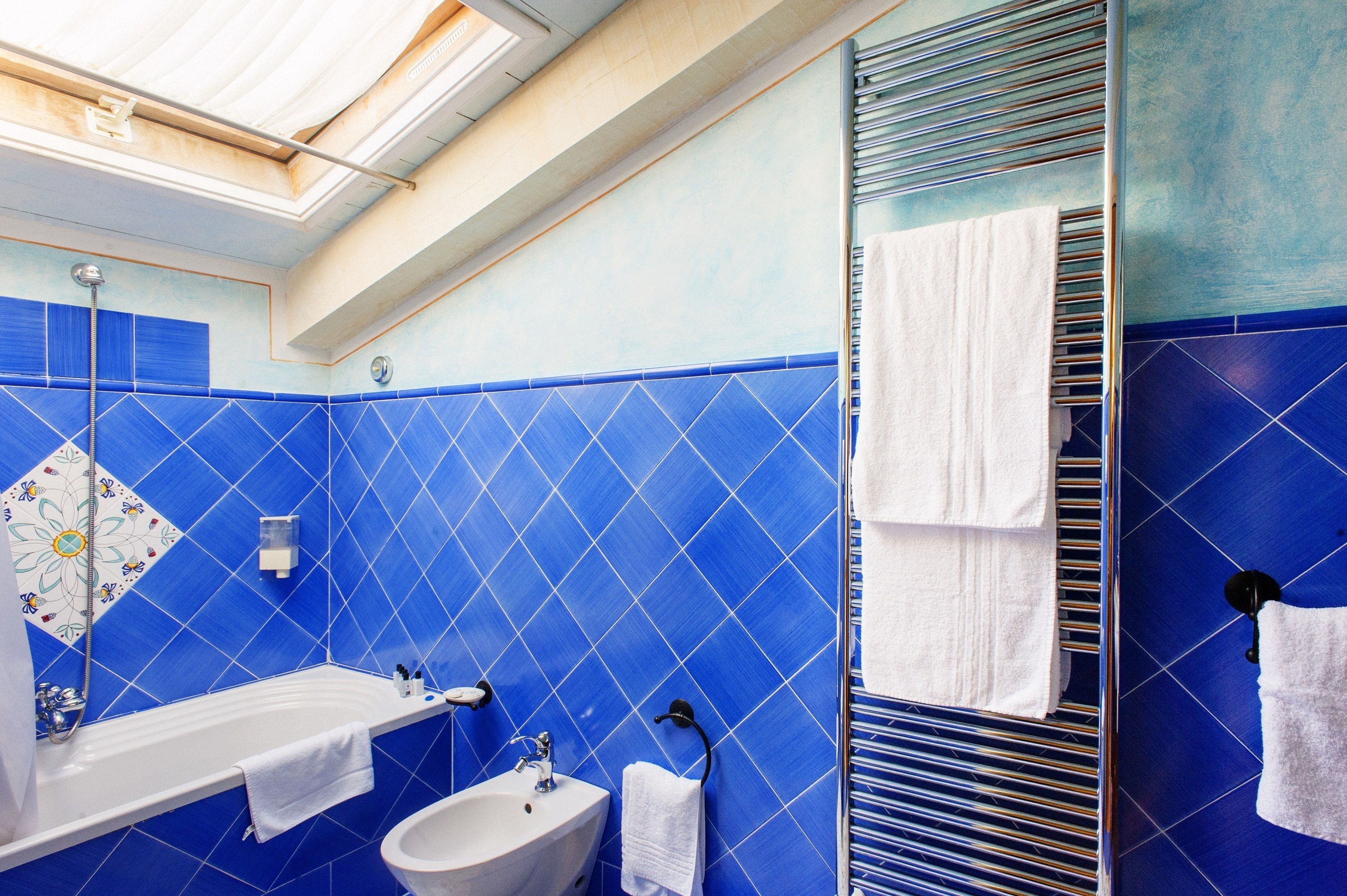 A bathroom with blue tiles, a bathtub, a sink, and a mirror.