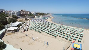 A beach with rows of umbrellas and beach chairs, a volleyball net, and buildings in the background. - Residenza Sveva (Termoli)