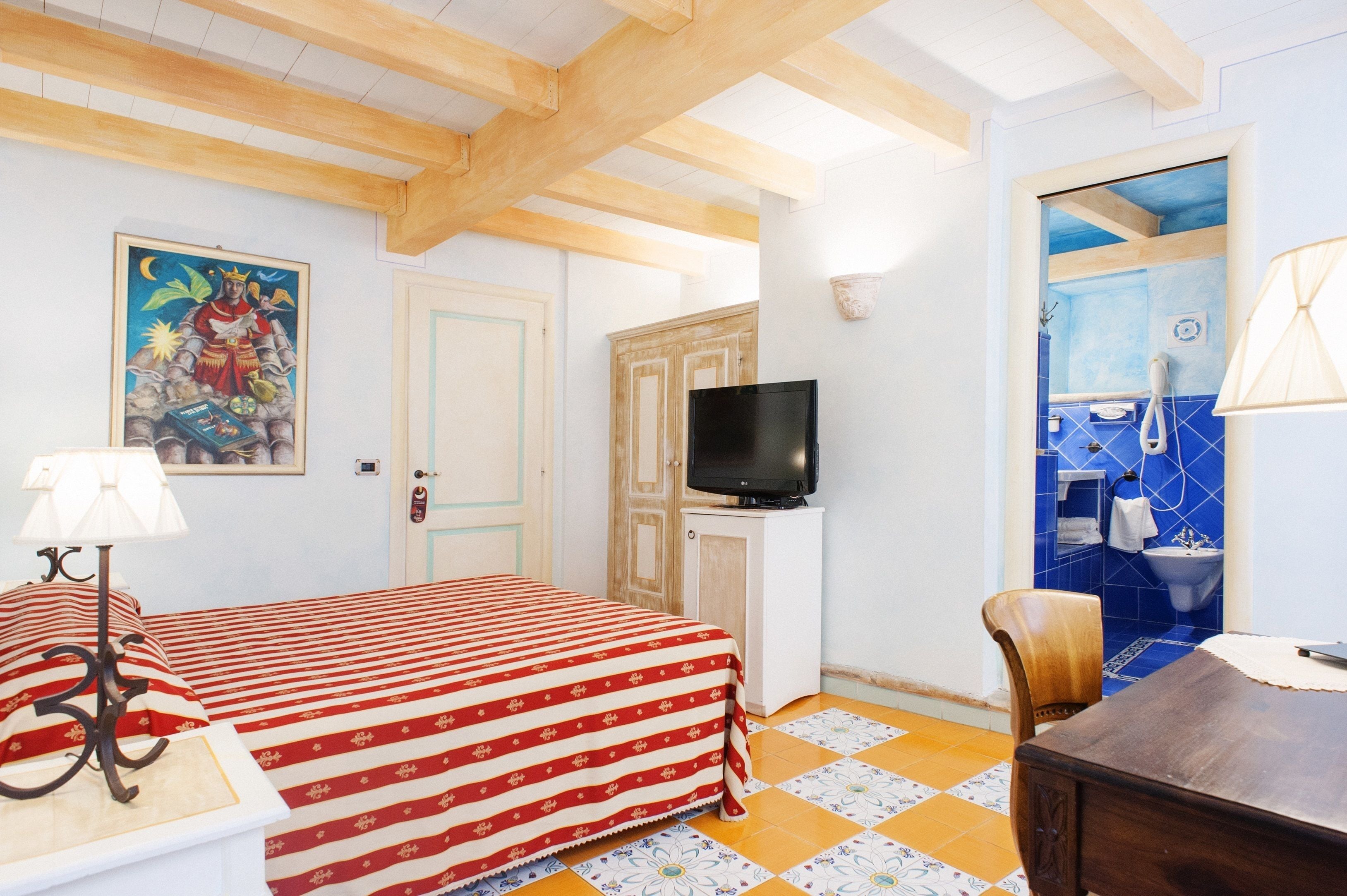 Ein Zimmer mit einem Bett, einem Fernseher, einem Holztisch und einem durchgehenden Türspalte sichtbaren Badezimmer.