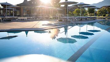Ein Pool mit sonnendurchfluteten Reflexionen, Sitzgelegenheiten im Freien und ein Gebäude im Hintergrund.