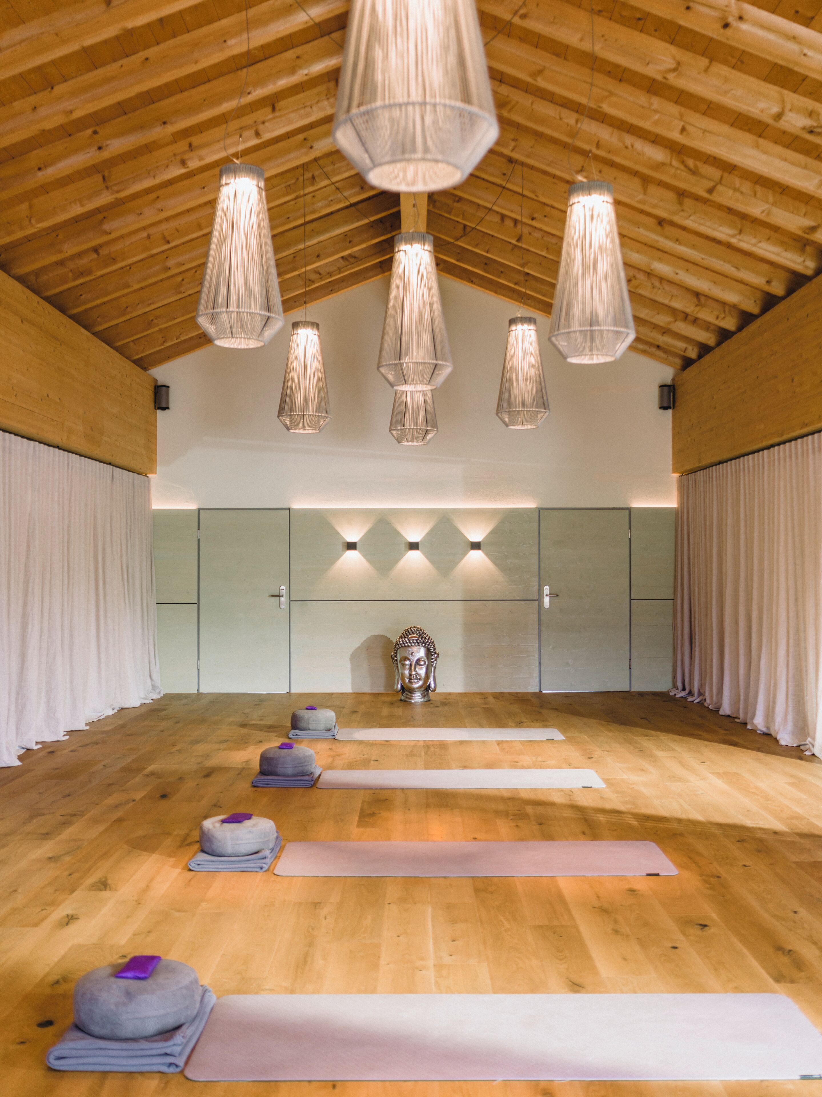 A spacious room with wooden flooring, a large mirror, and a meditation area with mats and a statue.