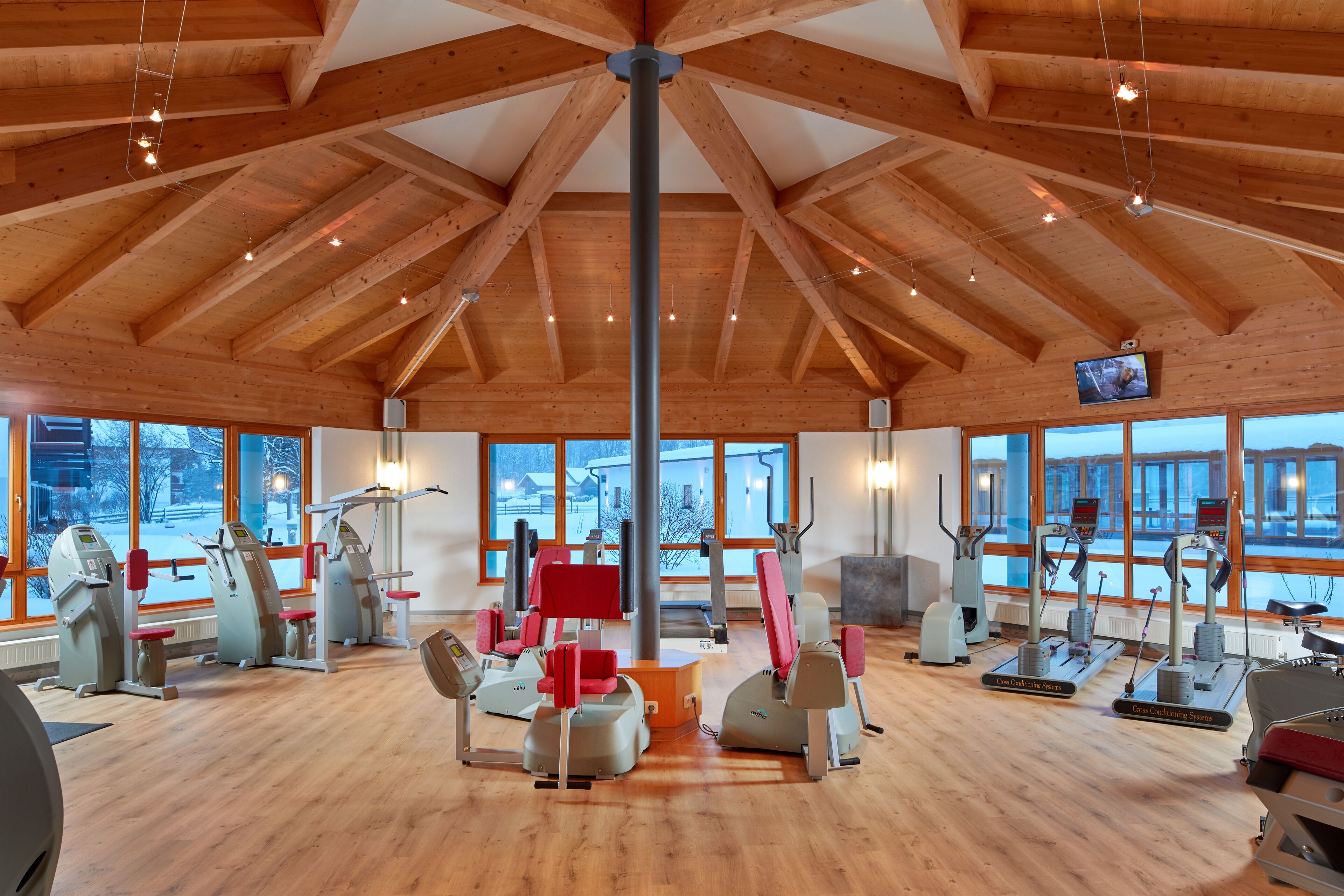 Ein Fitnessstudio mit verschiedenen Trainingsgeräten, gro ßen Fenstern und einer Holzbalkendecke.