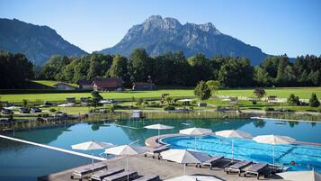 A swimming pool with lounge chairs and umbrellas, surrounded by a landscaped area with a mountain backdrop.