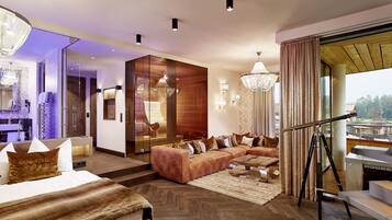 A modern hotel room with a large bed, a sofa, a fireplace, and a view of the outdoors.