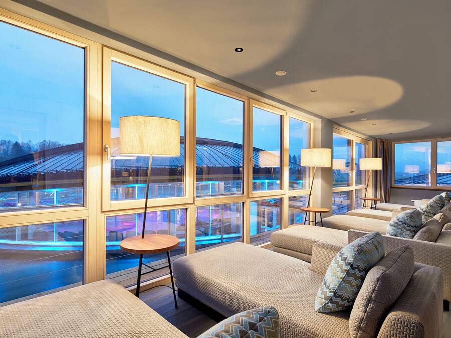 Um saguão de hotel moderno com grandes janelas, assentos confortáveis e vista para a piscina.