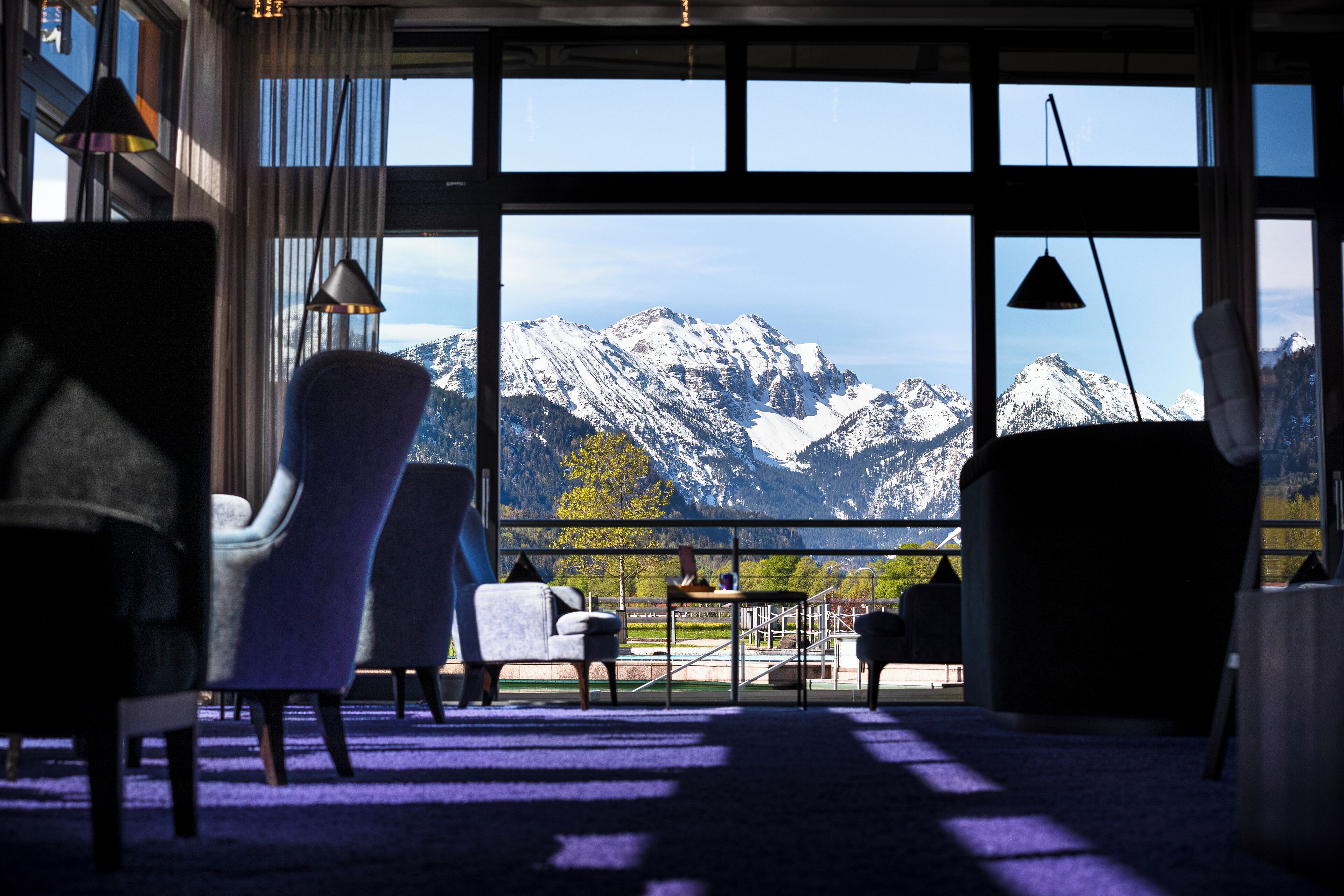 A room with a large window offering a mountain view, furnished with chairs and a small table.
