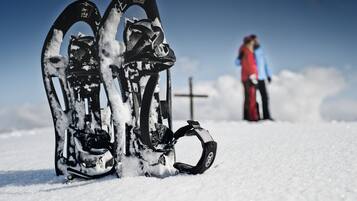 Ein Paar Schneeschuhe in einer verschneiten Landschaft, im Hintergrund ein Kreuz.
