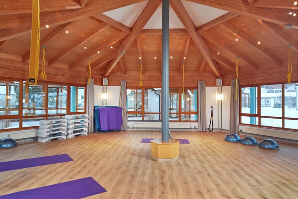A spacious room with wooden beams, large windows, and exercise mats.
